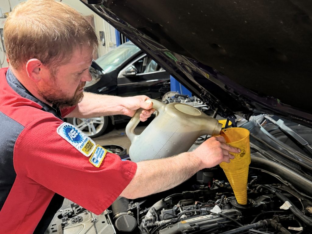 Mike Dyer adding fluid during BMW maintenance service at Westgate High Tech Auto Care in Omaha, NE.